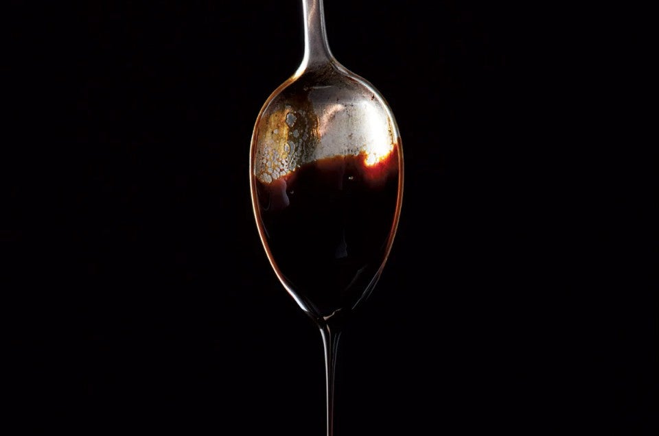 Molasses dripping off a spoon against a black background