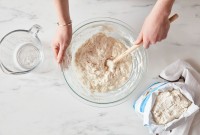 Baker mixing bread dough next to open bag of bread flour