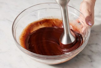 A baker using an immersion blender to make smooth chocolate ganache