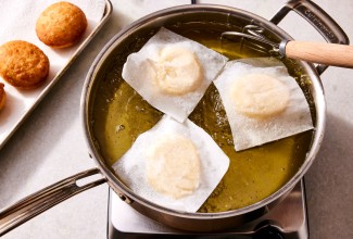 Doughnuts being fried on squares of parchment paper