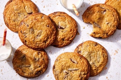 A few big chocolate chip cookies on a kitchen counter with glasses of milk